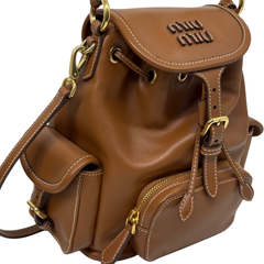 Brown leather backpack front close-up with flap stitching, embossed Miu Miu logo, and side strap.