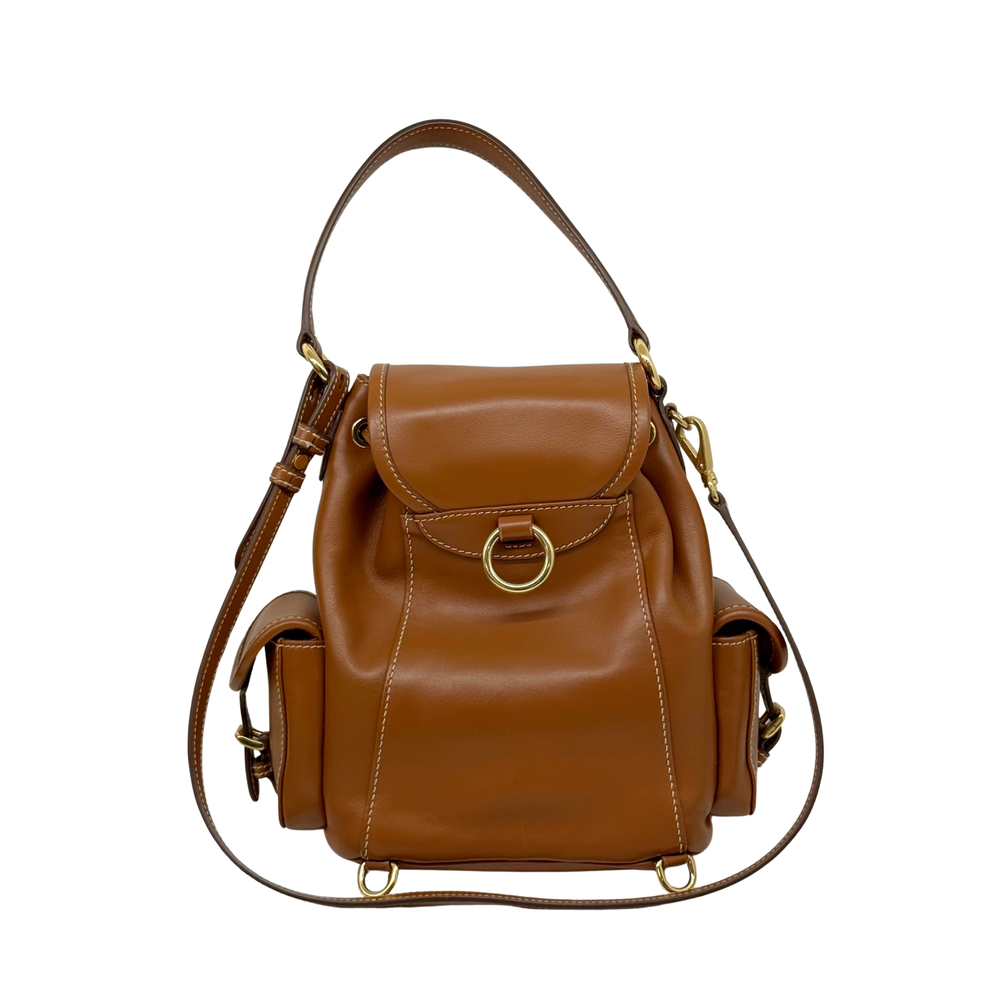 Brown leather mini backpack with front flap, drawstring details, and adjustable shoulder straps.