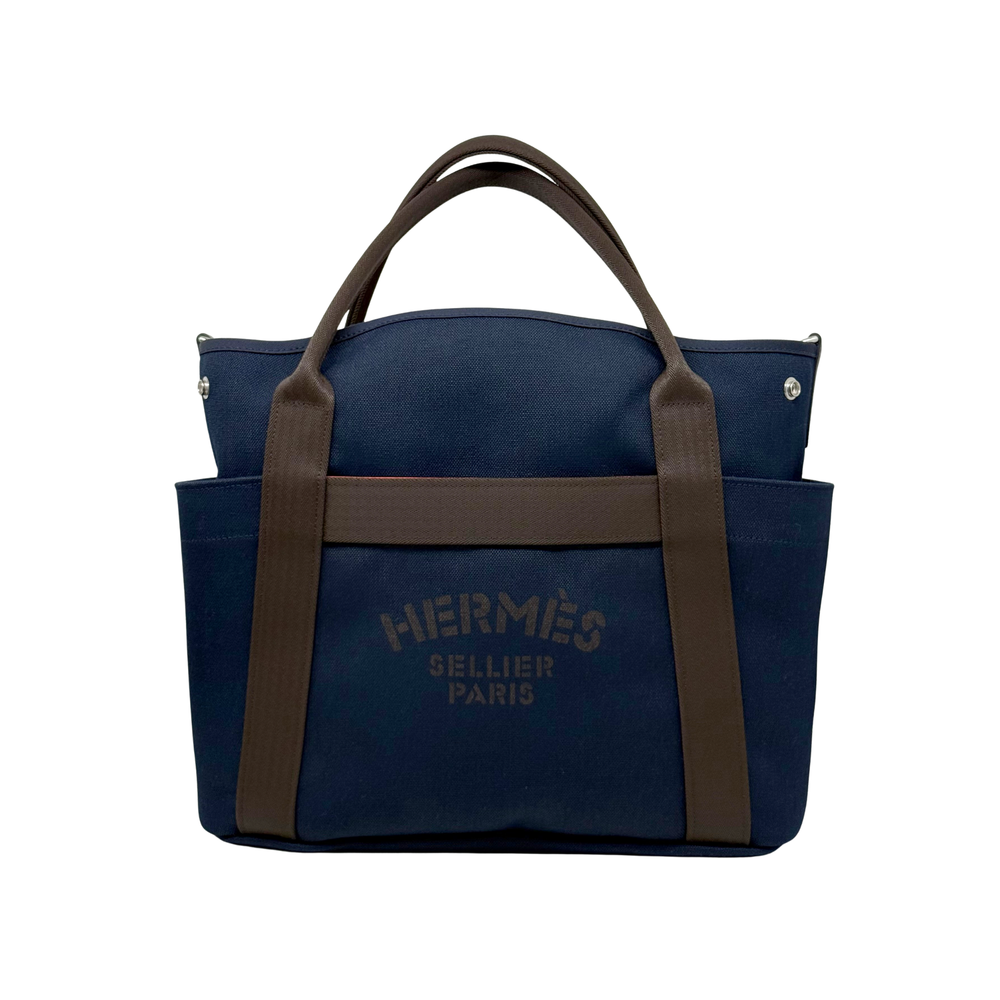 Hermes blue canvas satchel tote with brown handles, front band, and metal corner studs