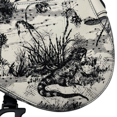 Christian Dior saddle bag toile panel close-up with detailed black animal and grass illustration.