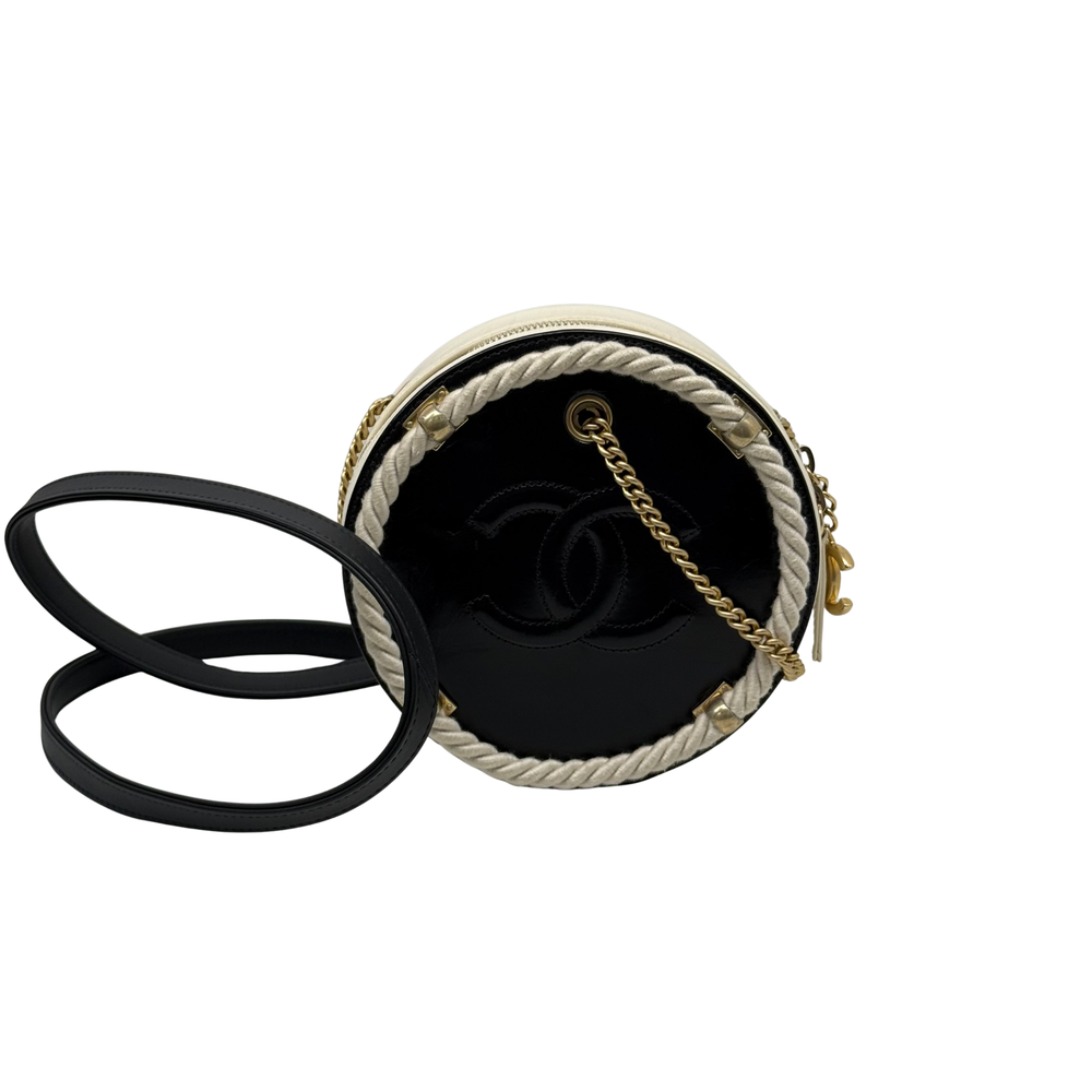 Cream round crossbody bag with braided trim, black strap, gold hardware and clasp