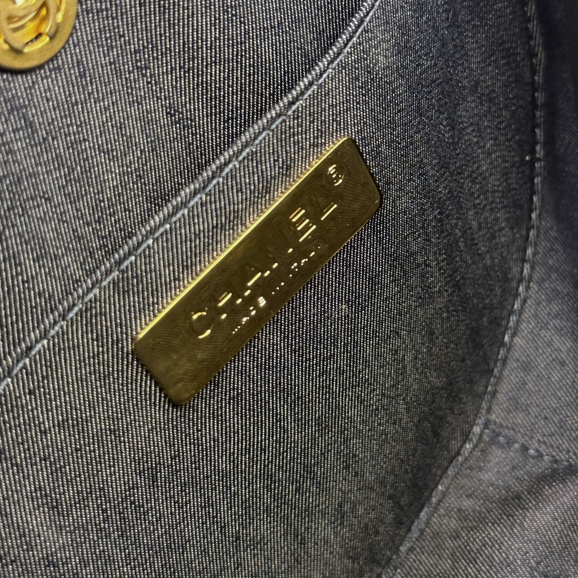 Close-up of Chanel round bag exterior label plate on dark textured leather