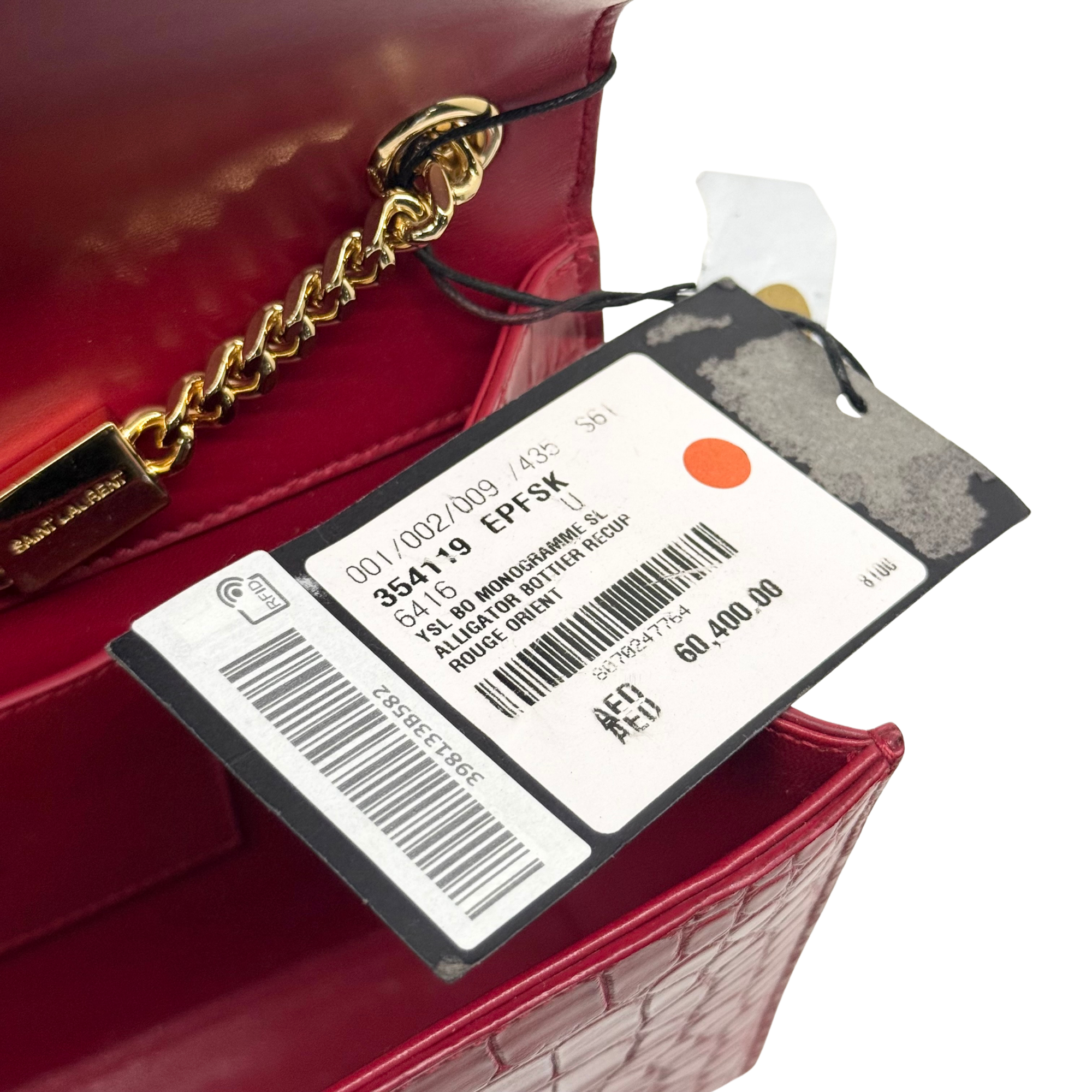 Red croc-textured flap clutch with gold chain strap, tags, and interior label
