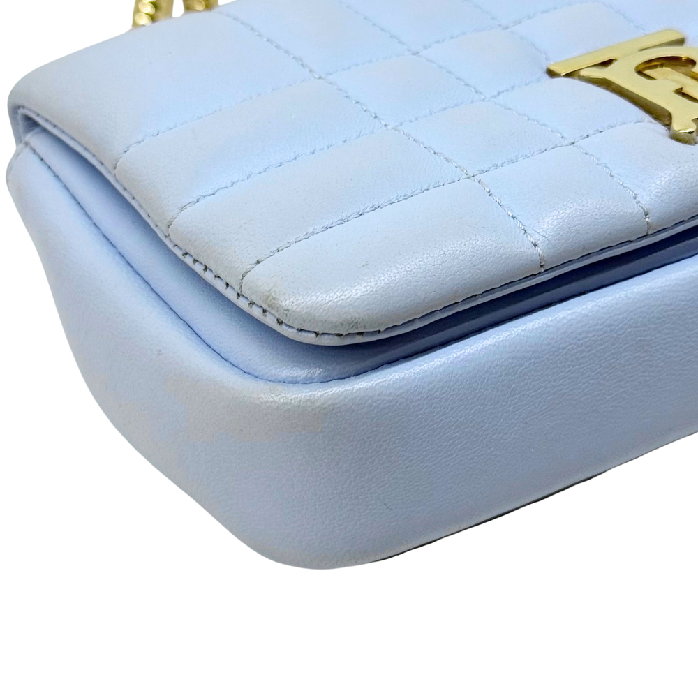 Light blue quilted leather bag with gold edge clasp hardware and curved top.