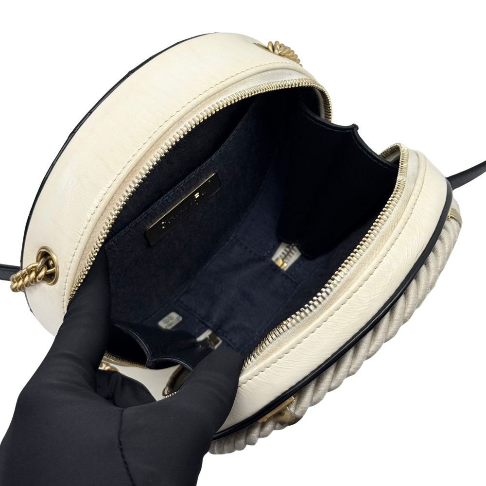 Open cream round crossbody bag with braided edge trim, black lining, gold zip pulls