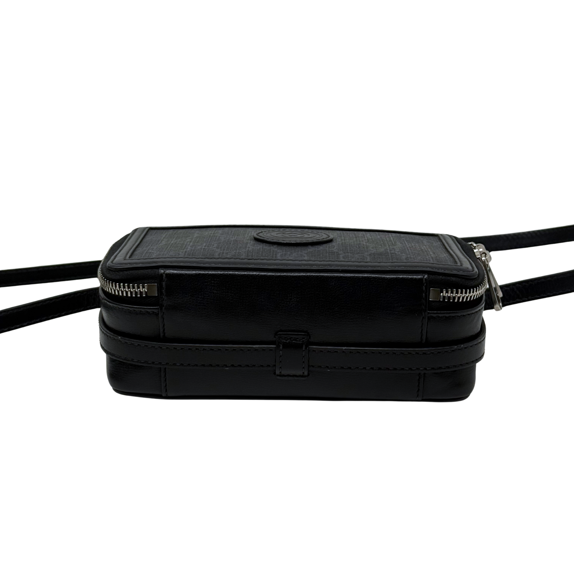 Small crossbody bag front, black leather body and round logo plaque, zip top