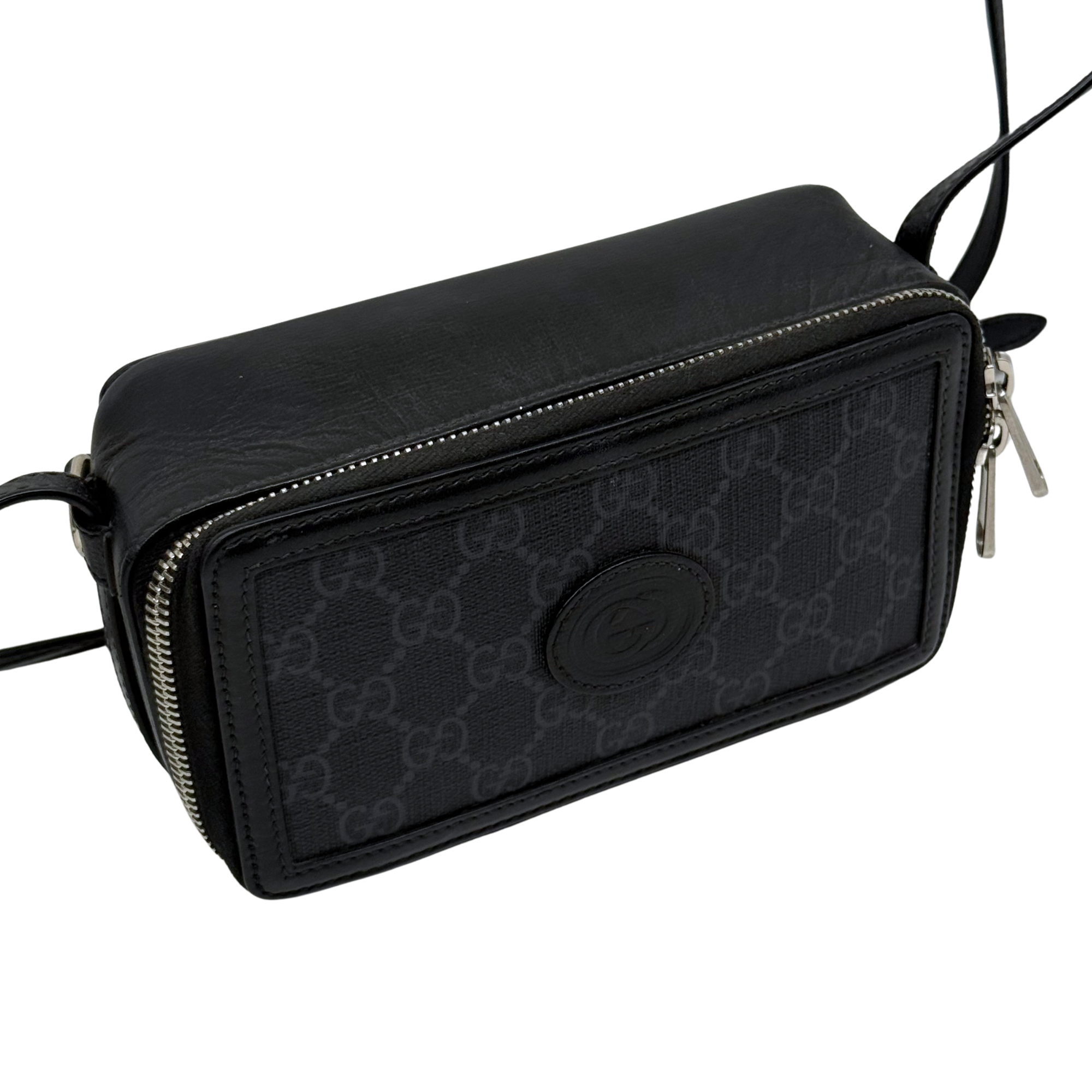 Small crossbody bag side view, black GG canvas with round logo emblem and zipper