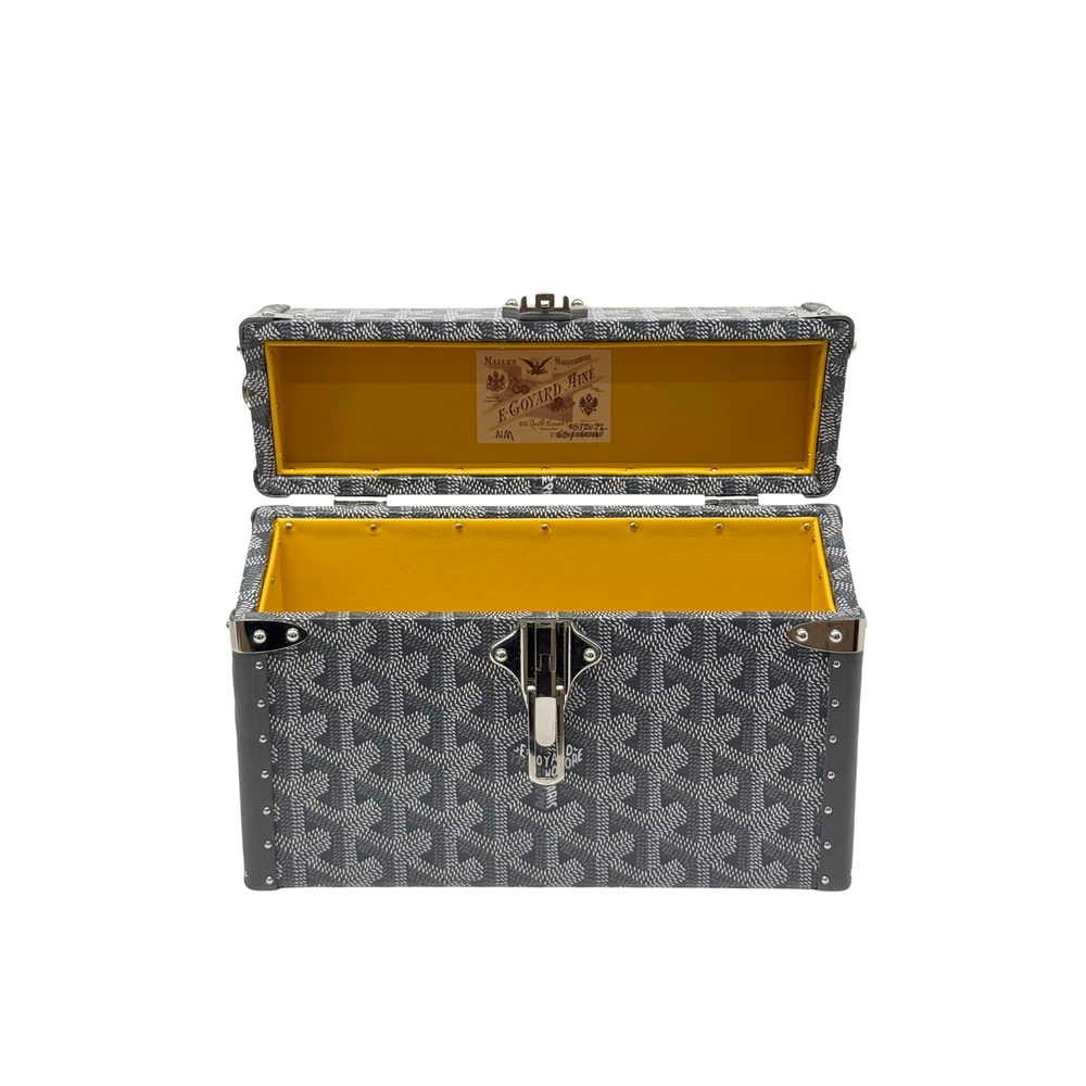 Goyard mini trunk opened to show yellow interior and front lock on patterned fabric