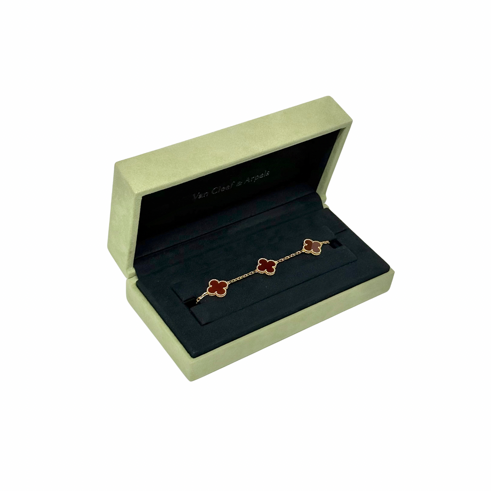 Goldtone bracelet with red clover motif links on dark display cushion