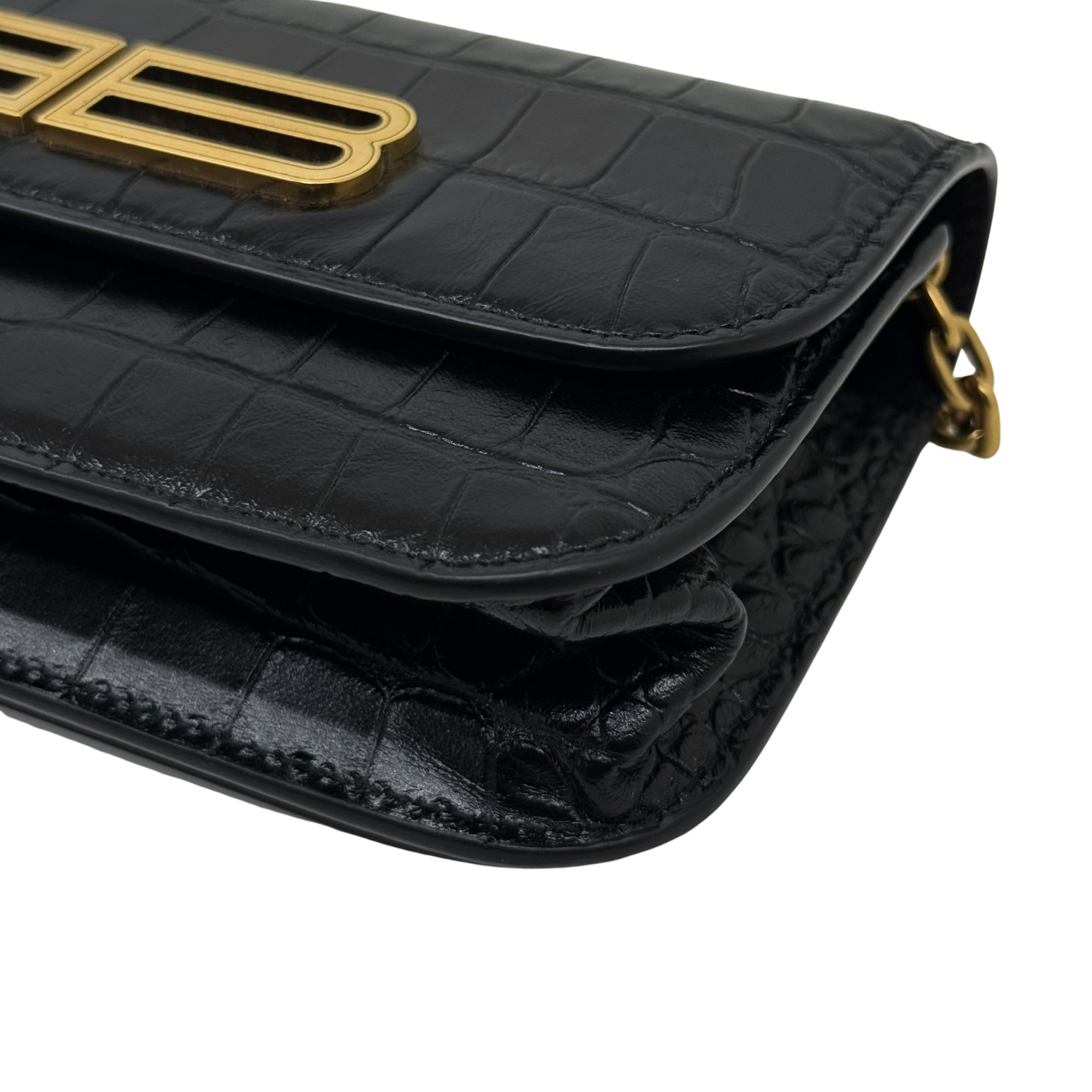 Black croc-embossed leather flap edge with gold ring hardware and stitched trim detail.