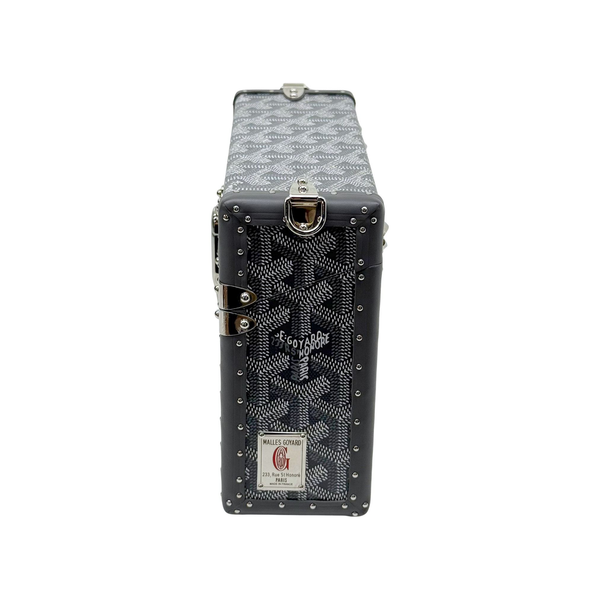 Goyard mini trunk with front lock, studded black corners, and hanging brand tag label