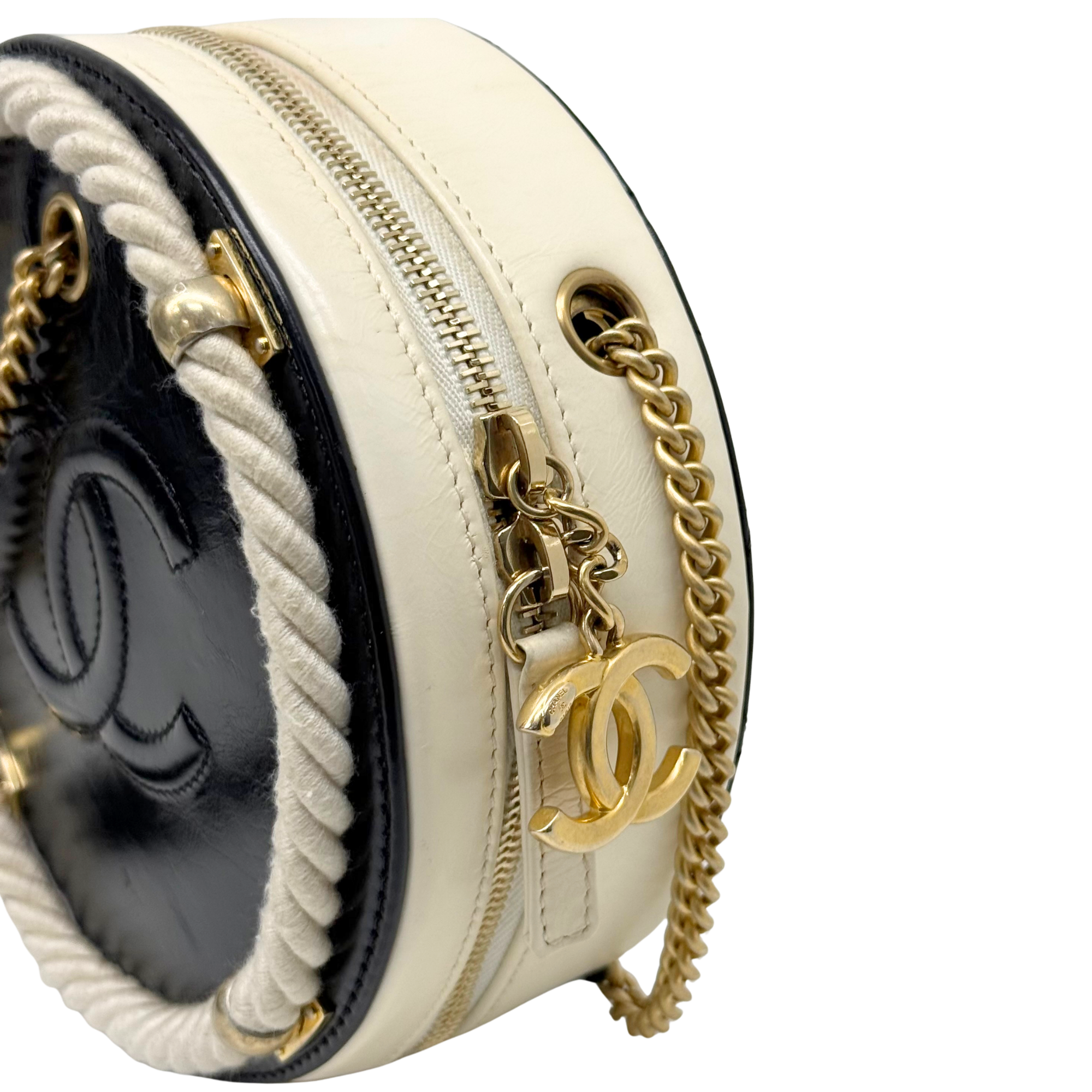 Side view of cream round bag with gold chain strap, braided trim, and CC charm
