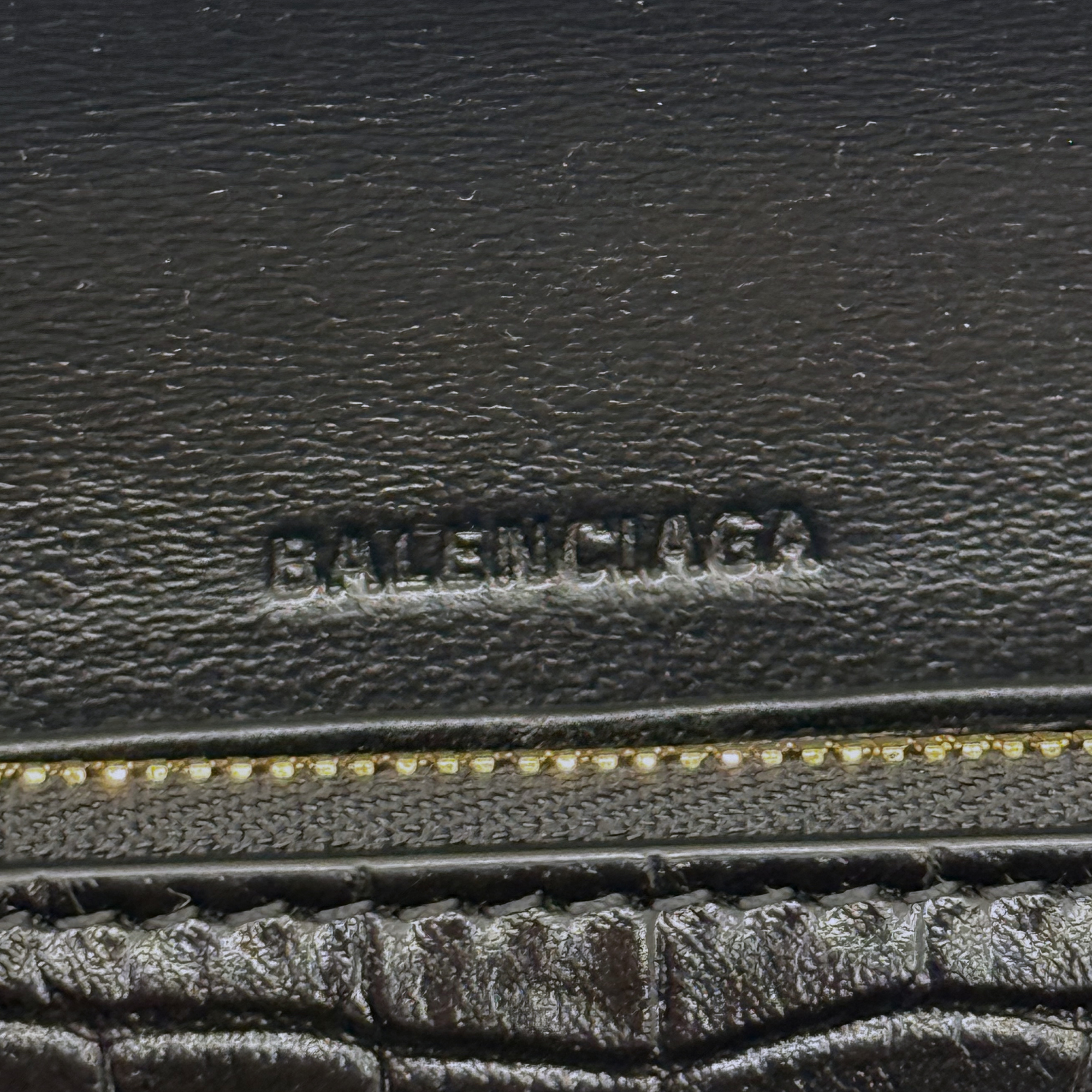 Black leather emboss logo stamp with gold-tone zipper track detail on bag interior.