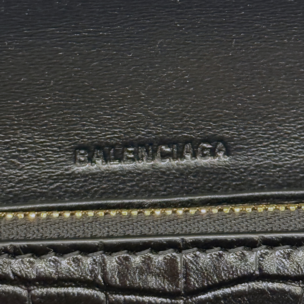 Black leather emboss logo stamp with gold-tone zipper track detail on bag interior.