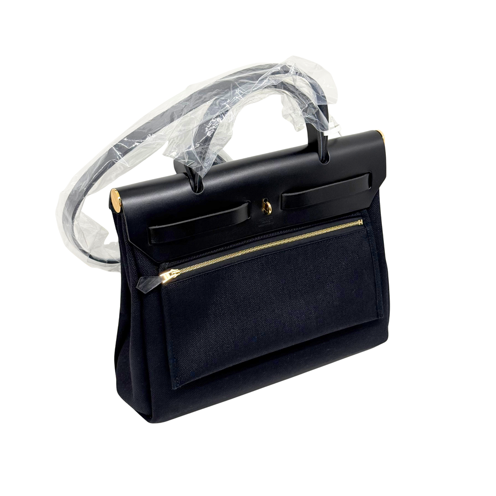 Hermes black leather handbag with front flap, gold zipper, and protective plastic cover