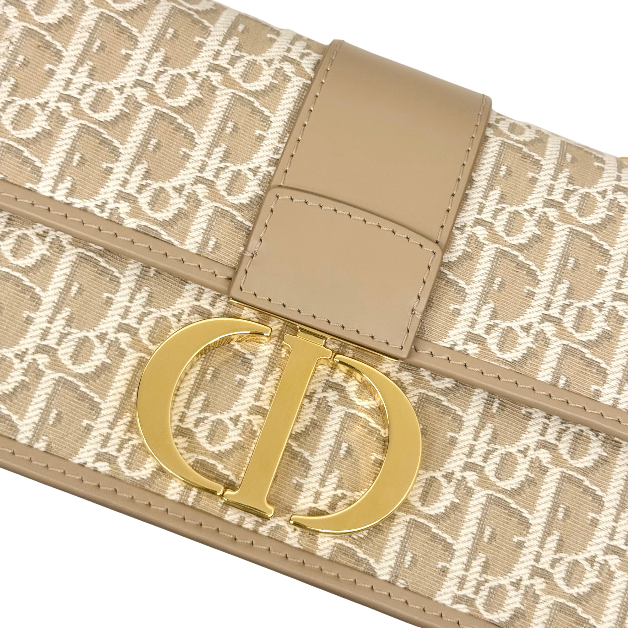 Dior pre-owned bag showing gold "D" logo plaque on beige monogram canvas