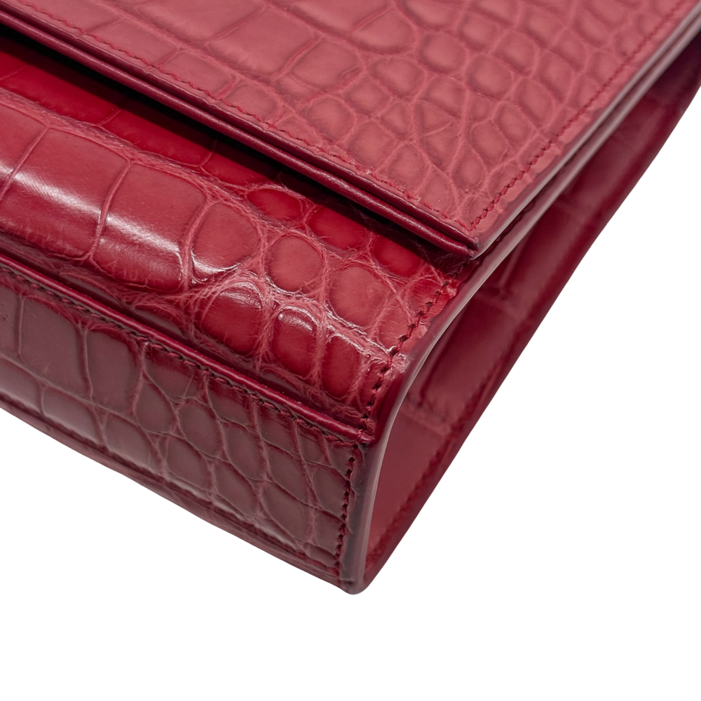 Red crocodile-embossed leather flap bag corner with gold-tone trim and stitching detail