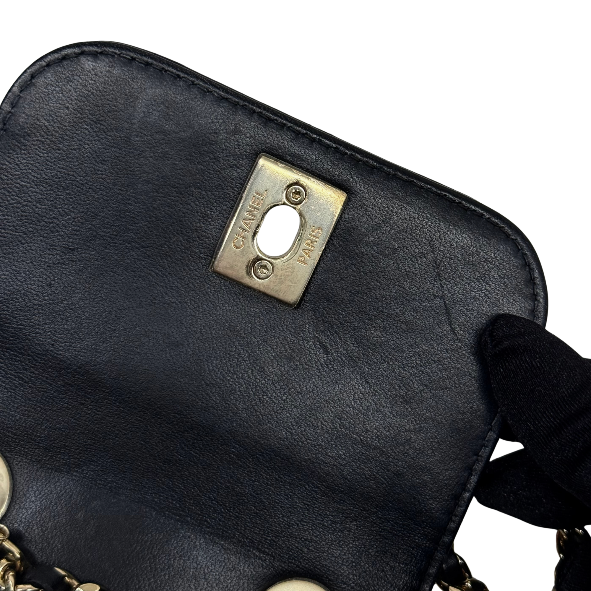 Black Chanel leather flap bag close-up of gold Chanel plate and ring pull