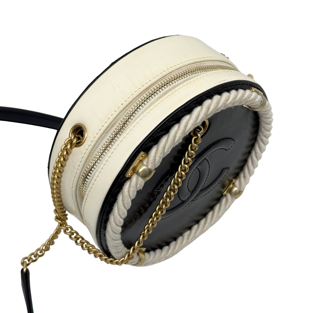 Cream round mini bag with black interior, gold chain strap, and zip top closure.