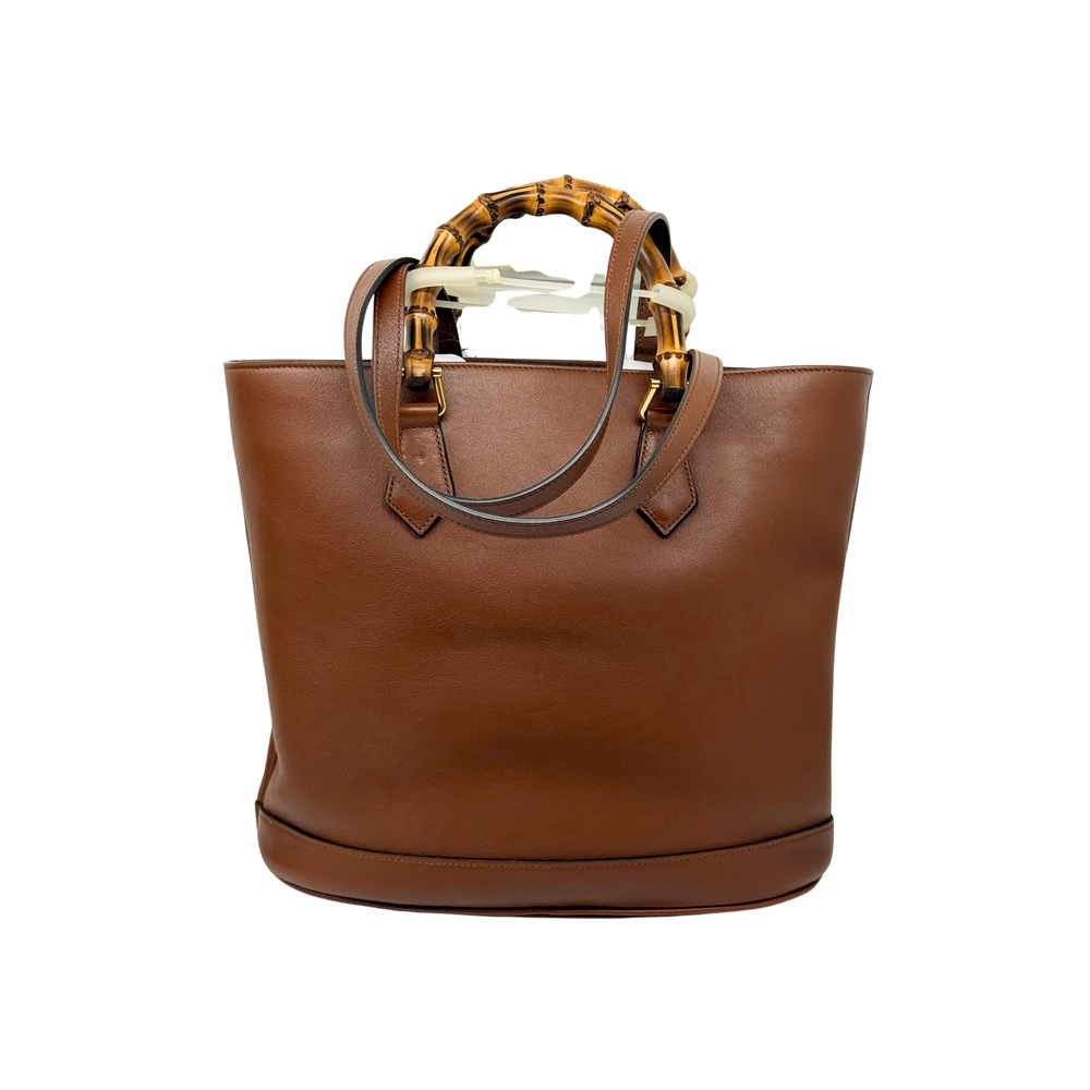 Brown leather tote bag with curved top and bamboo-style handle straps