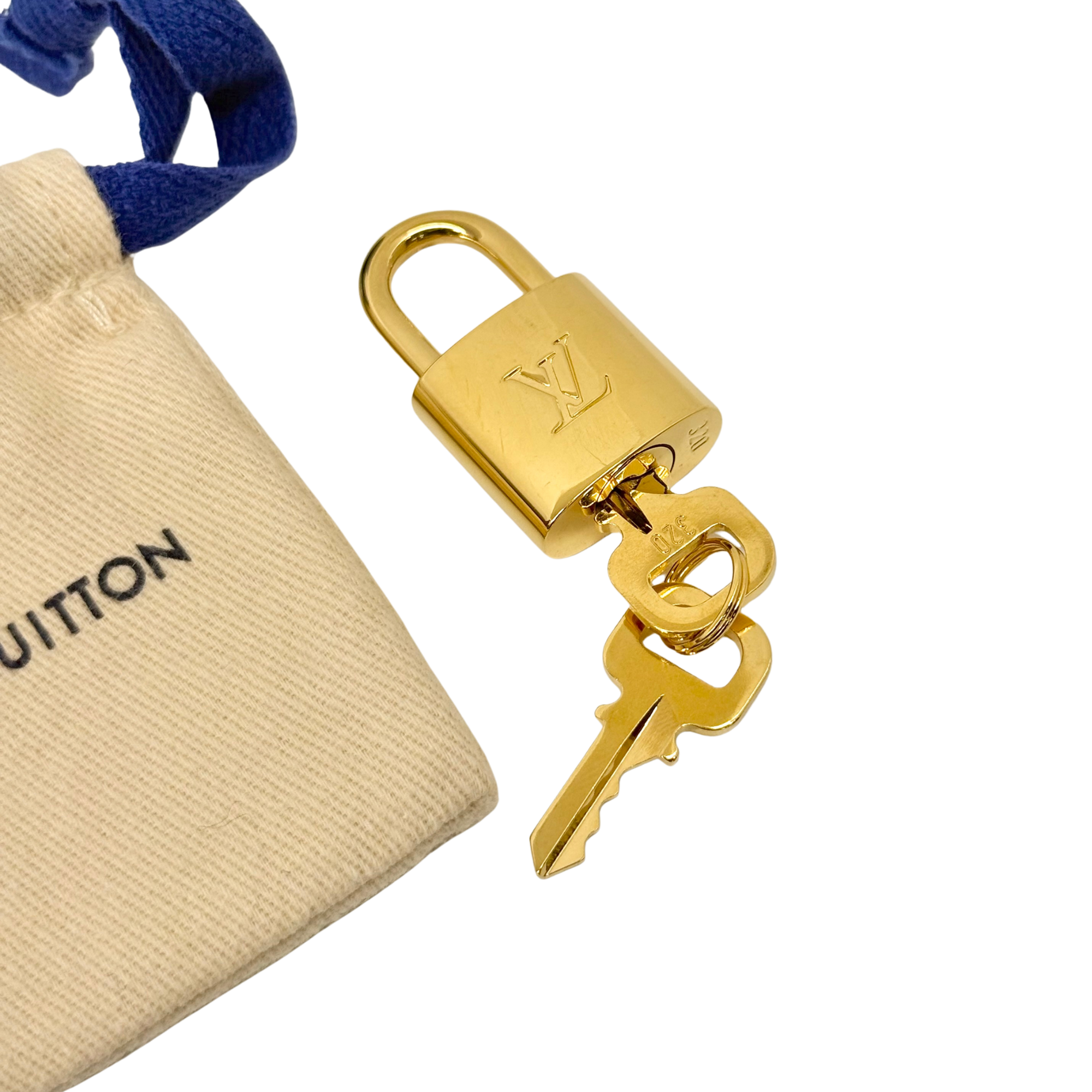 Gold key ring with two keys and Louis Vuitton logo, next to a fabric pouch