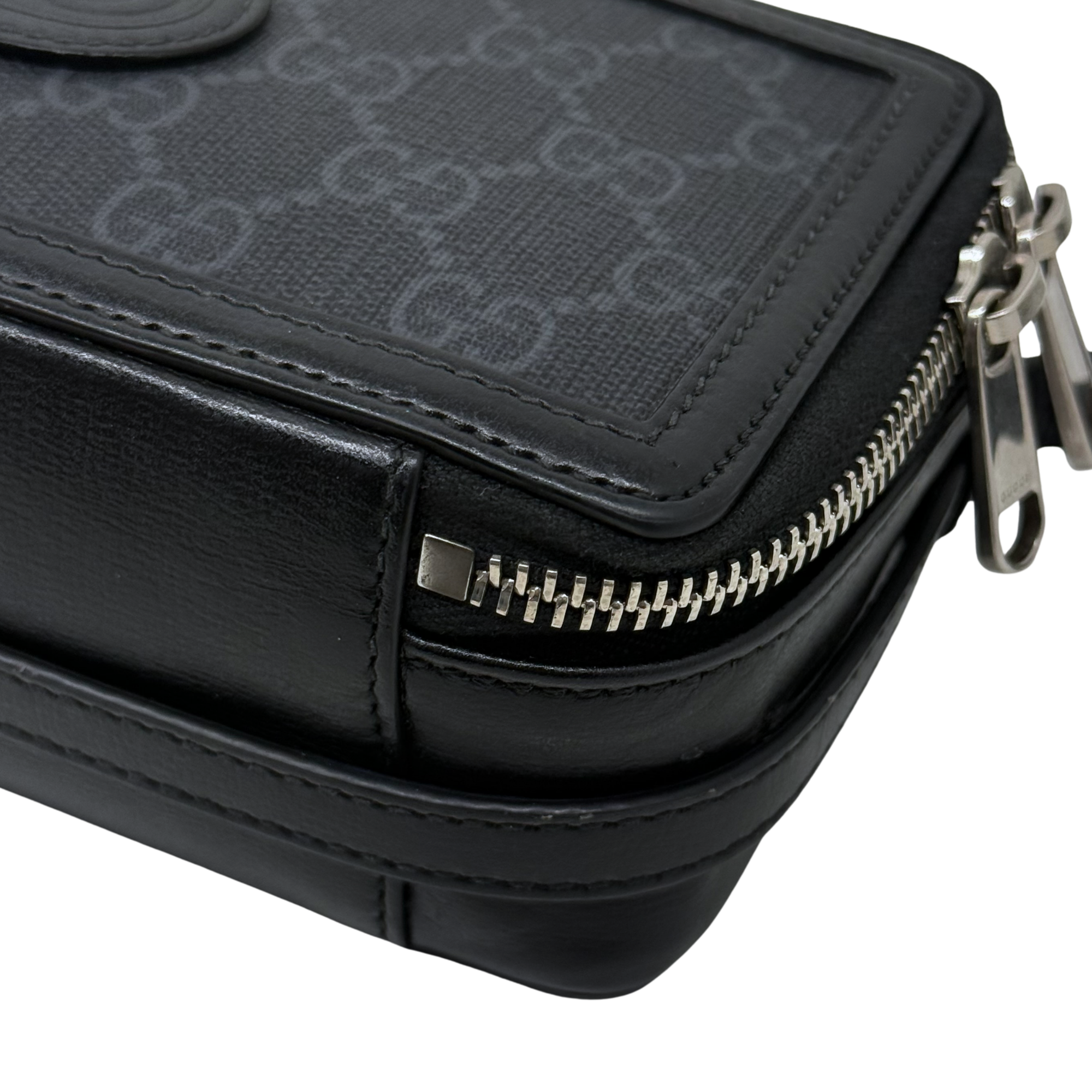 Small crossbody bag detail, metal zipper pull and front seam, black leather