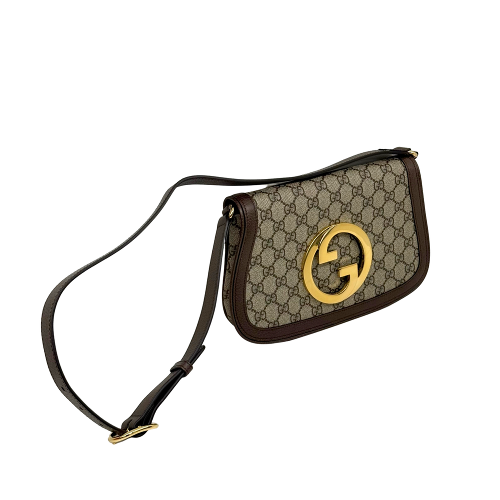 Gucci GG canvas crossbody bag with brown leather trim, gold G emblem, and long strap
