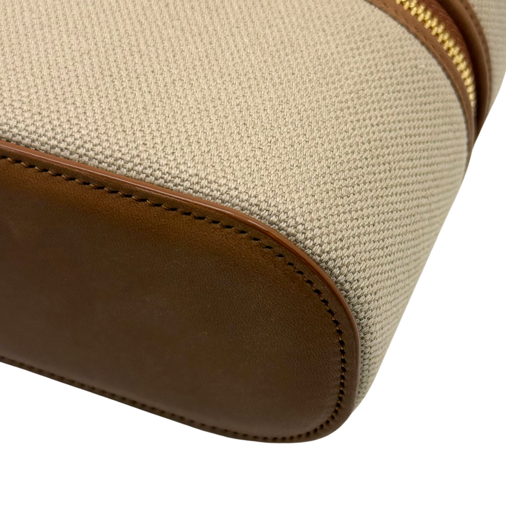 Rounded corner of beige vanity bag with brown leather piping and stitched seam