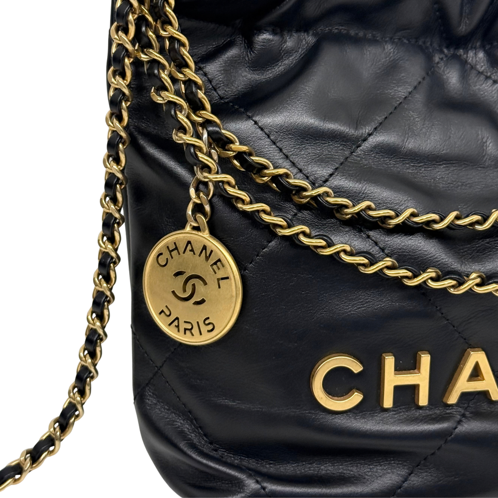 Black quilted mini crossbody bag with gold chain strap and round Chanel logo charm.