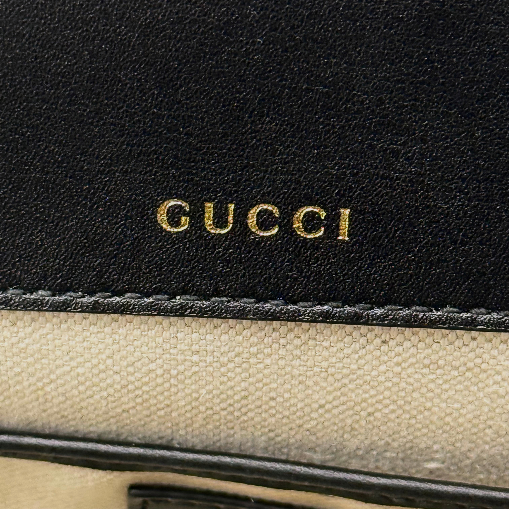 Gucci black leather exterior with embossed Gucci logo near beige fabric lining