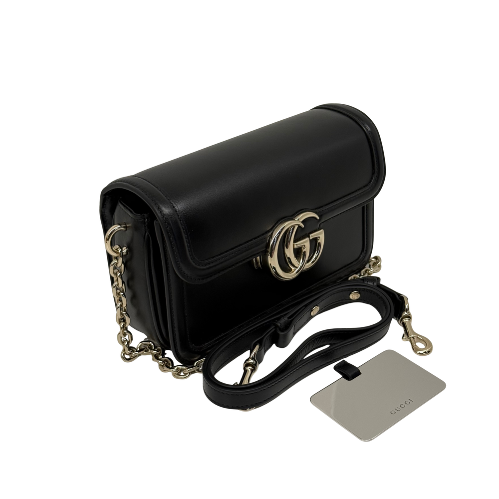 Black leather mini shoulder bag with gold-tone GG clasp, chain strap, and tag
