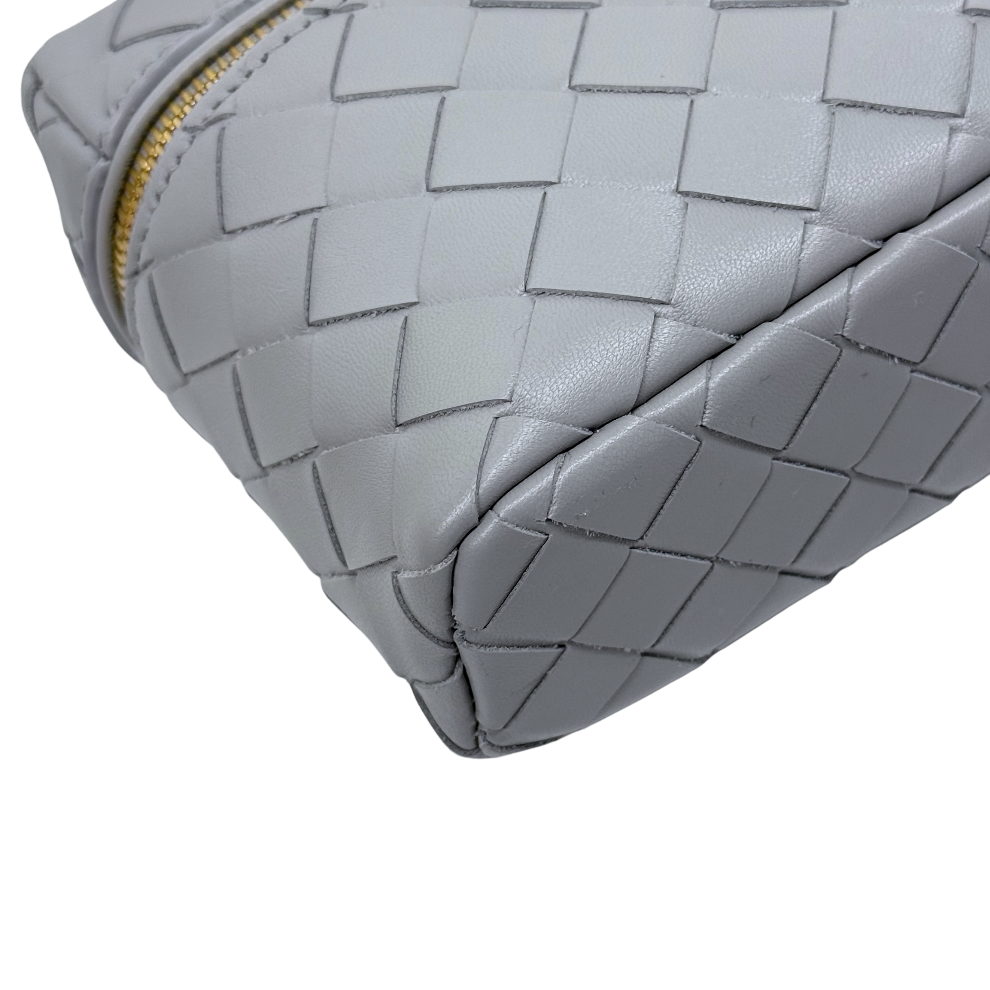 Bottega Veneta gray woven leather corner detail with rounded shape and gold zipper trim.