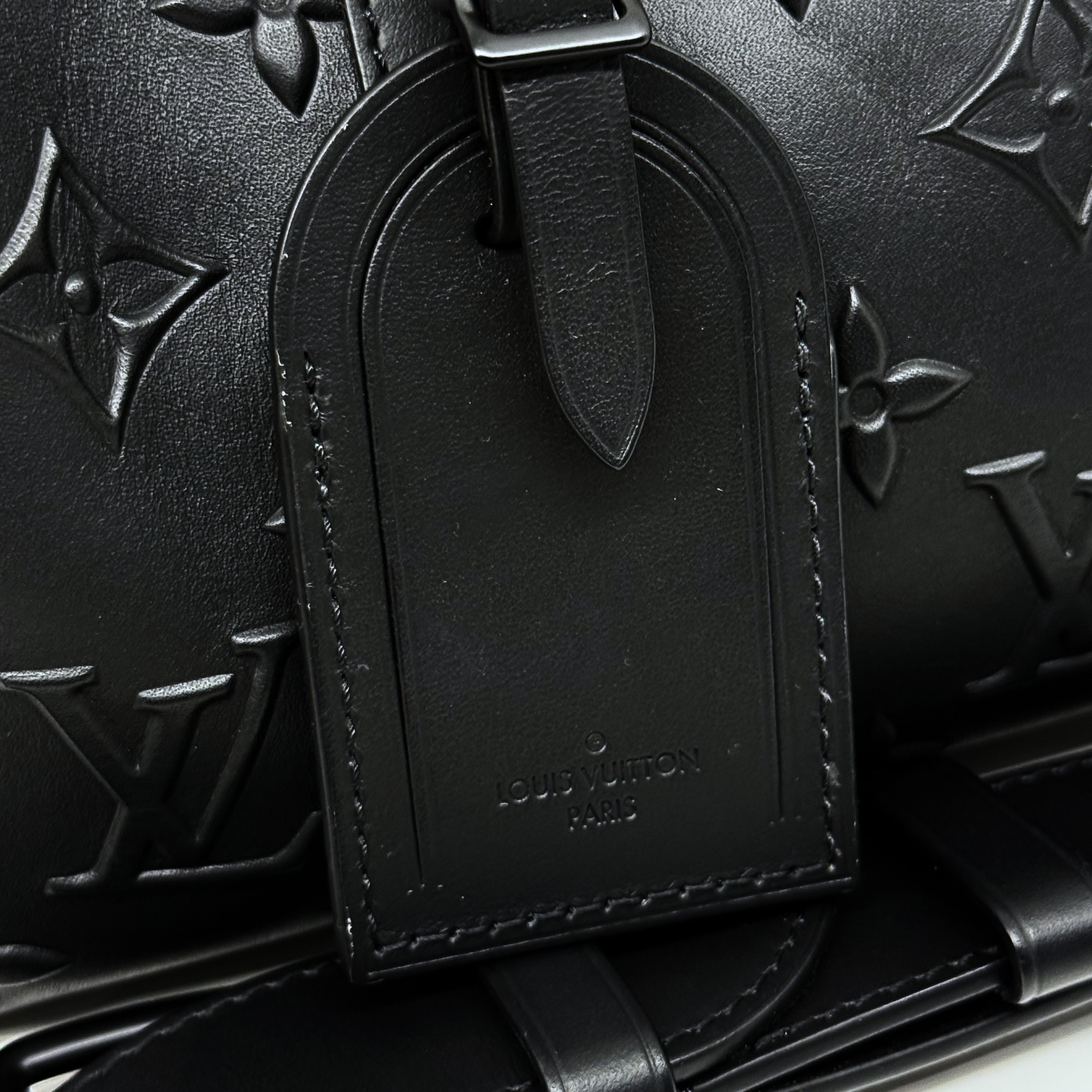 Louis Vuitton Paris embossed tag on black monogram crossbody bag, close-up