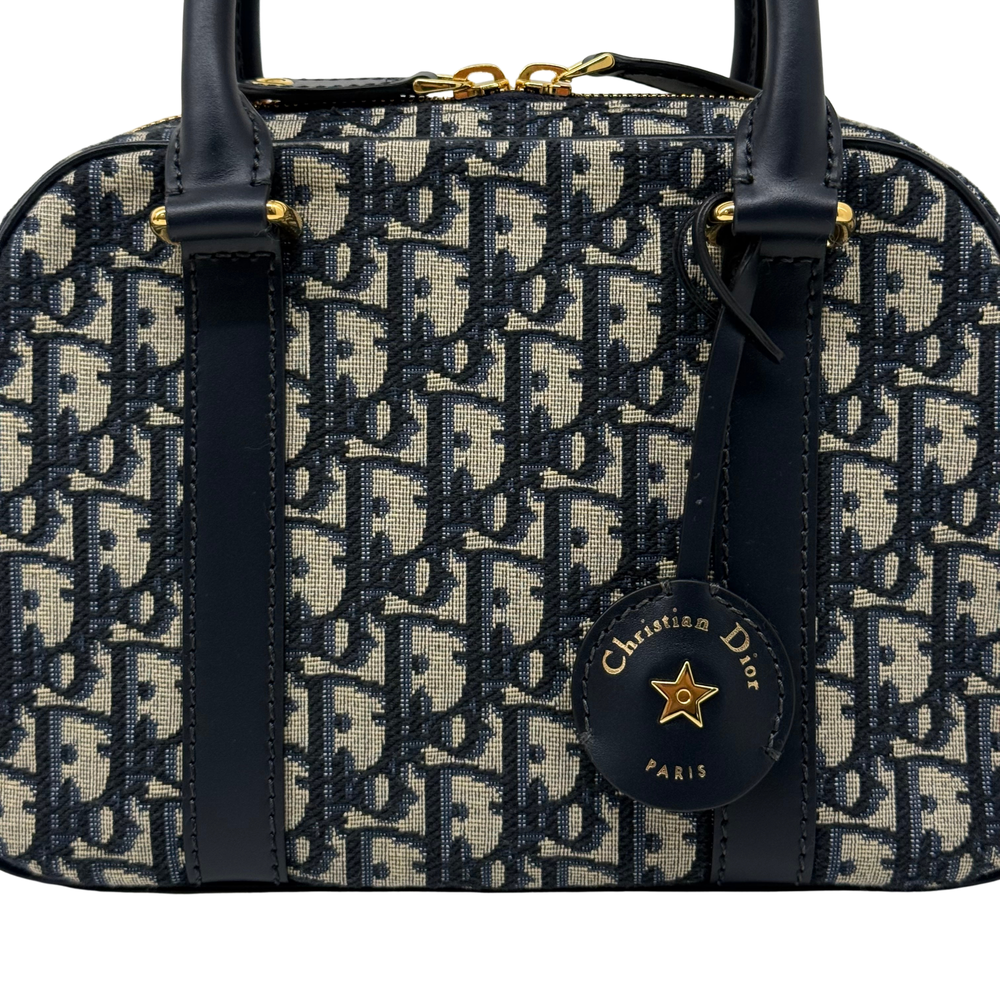 Dior monogram duffel bag with navy leather straps and front logo charm, gold accents