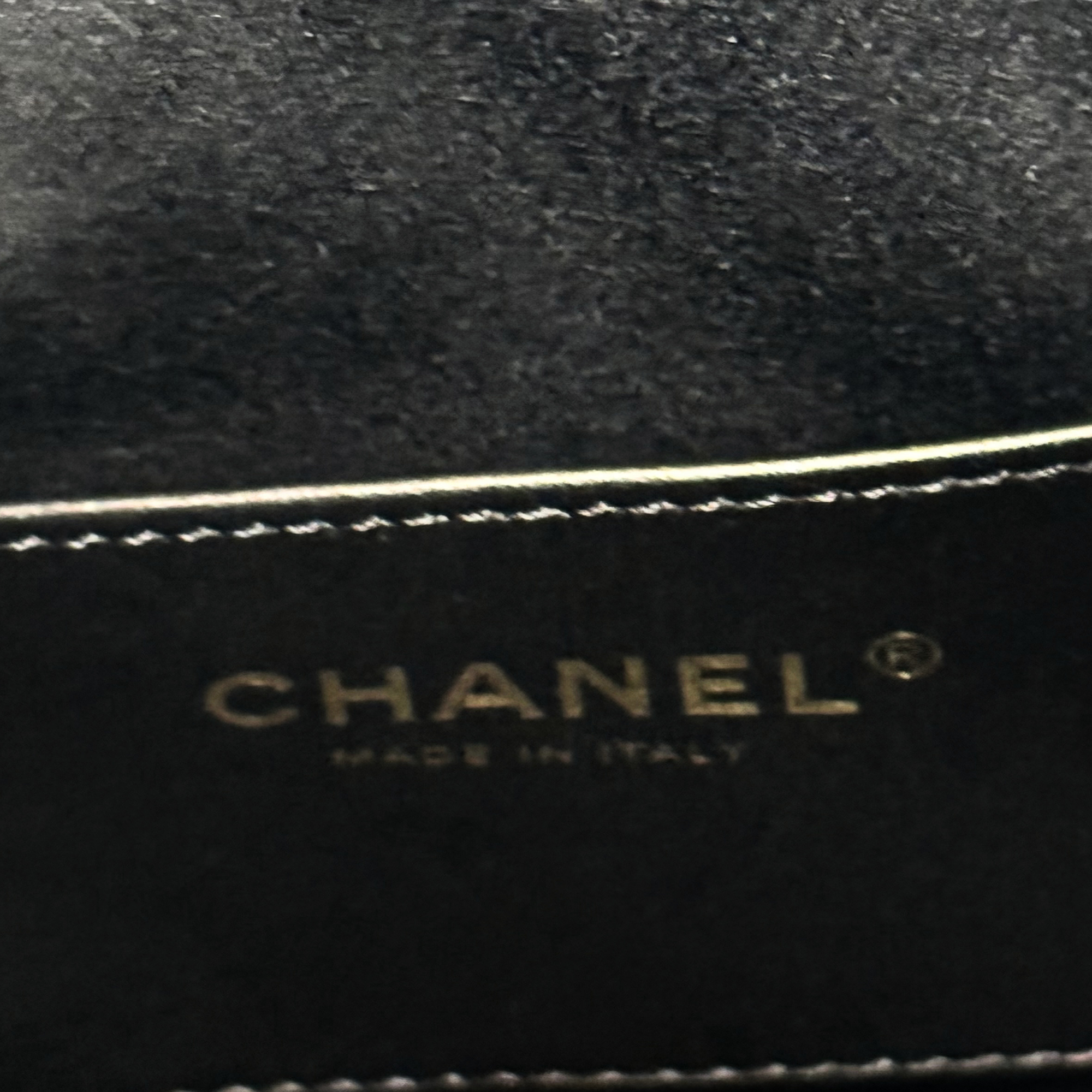 Black Chanel label with gold “CHANEL” text and stitched trim edge