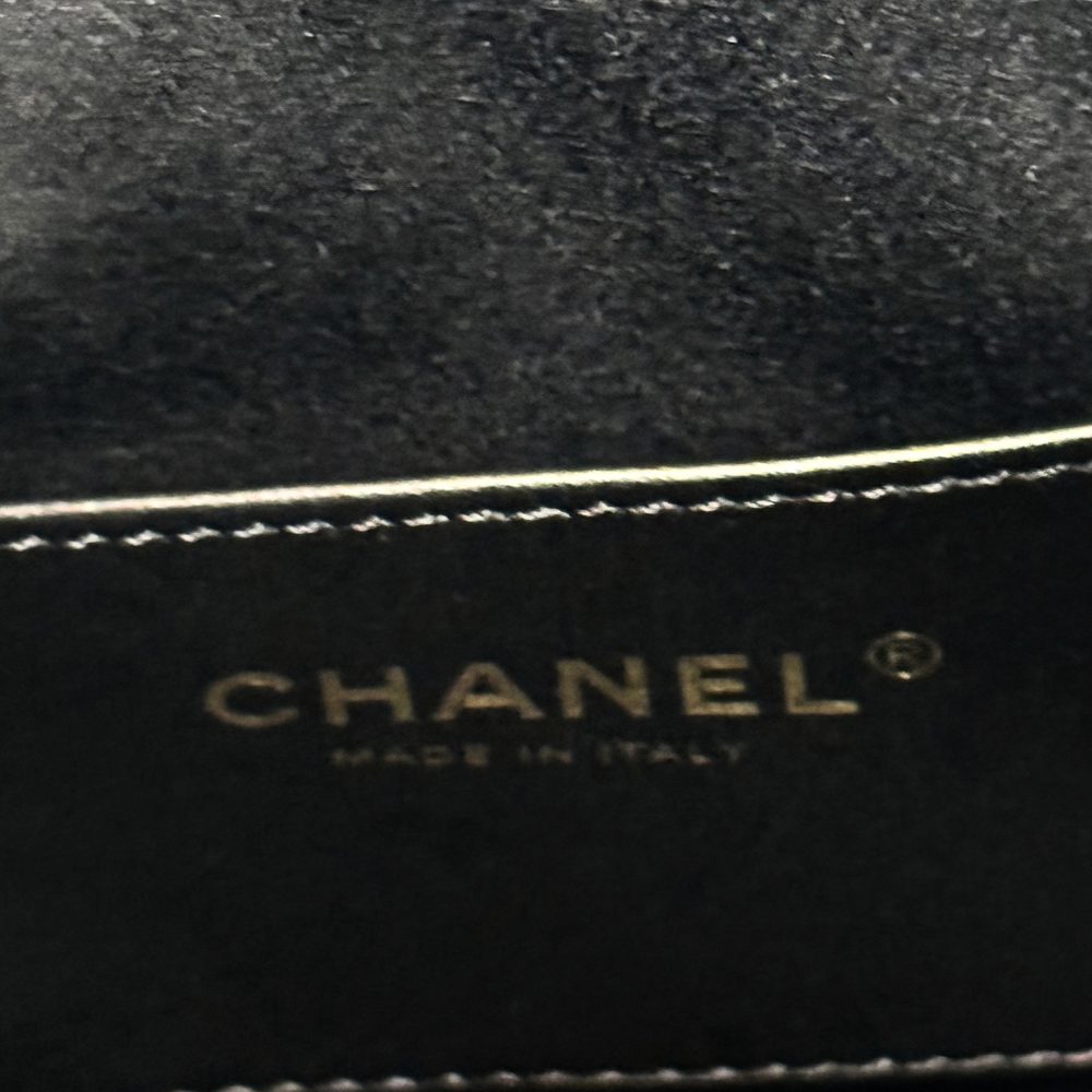 Black Chanel label with gold “CHANEL” text and stitched trim edge