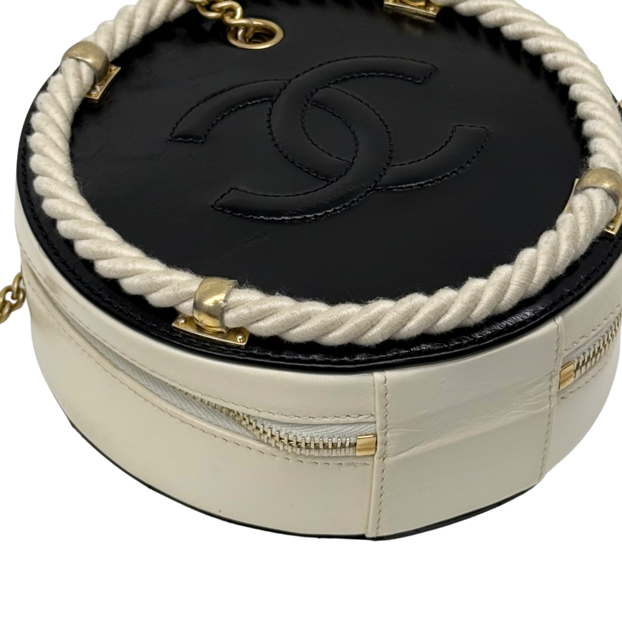 Close-up of cream round bag top with black CC-style logo patch and braided trim